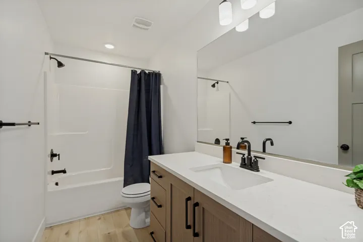 Wood-finish flooring, white solid surface countertop, wood vanity with black hardware, black fixtures, and white tub/shower combination