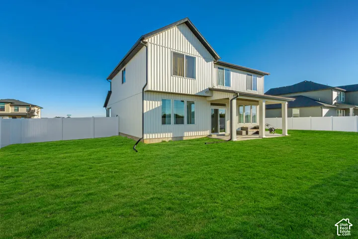 Expansive green lawn, white privacy fencing, covered patio, multiple large windows, and a modern exterior siding