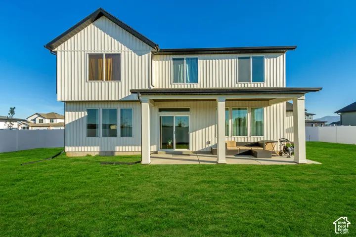 White vertical siding exterior with a covered patio, multiple windows, and a substantial grassy area