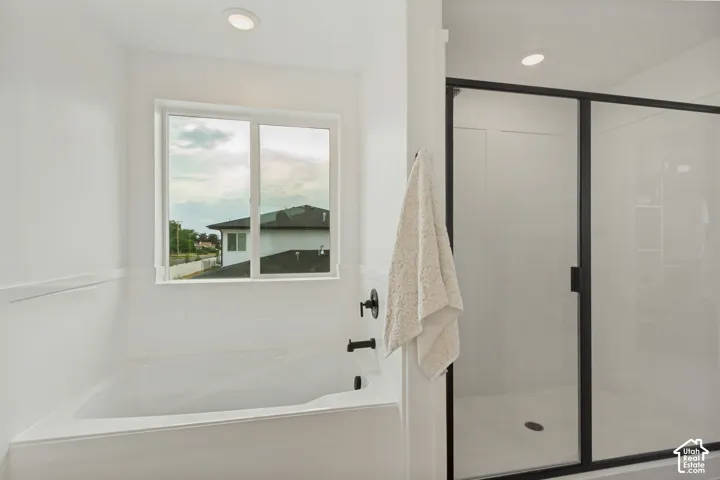Recessed lighting illuminates the modern white bathroom featuring a built-in tub with a matte black faucet and a separate shower enclosure with a black-framed glass door