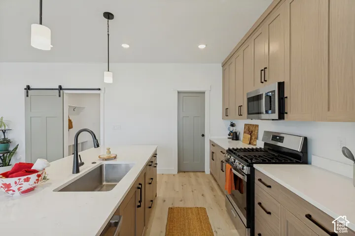Kitchen featuring a large island with an undermount sink and matte black faucet, light wood-finish cabinetry, stainless steel microwave, gas range, and wood-finish flooring