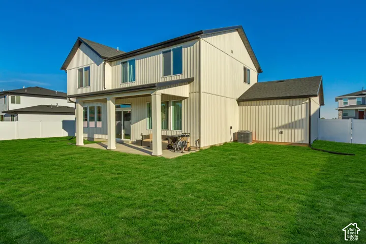 Expansive grassy yard with white privacy fencing, a covered patio, and a two-story exterior with vertical siding