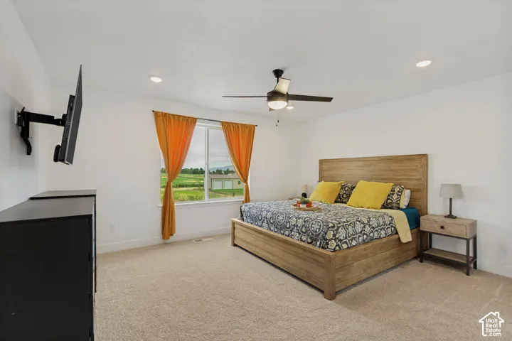 Recessed lighting, ceiling fan, expansive window, neutral carpet, and wood-finish bed frame