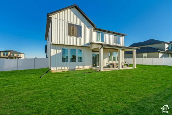 Expansive green lawn with a covered patio featuring robust pillars, a white privacy fence, and vertical panel siding