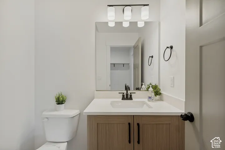 Vanity with wood-finish cabinetry, white countertop, rectangular undermount sink, and matte black faucet