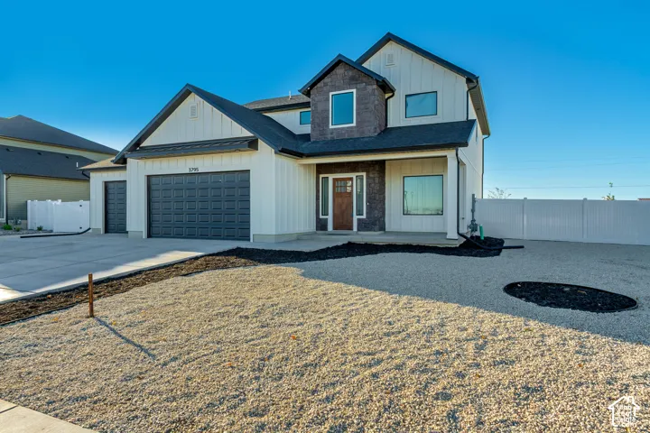 Contemporary two-story exterior with vertical siding, dark stone accents, wood-paneled entry door, and a two-car garage