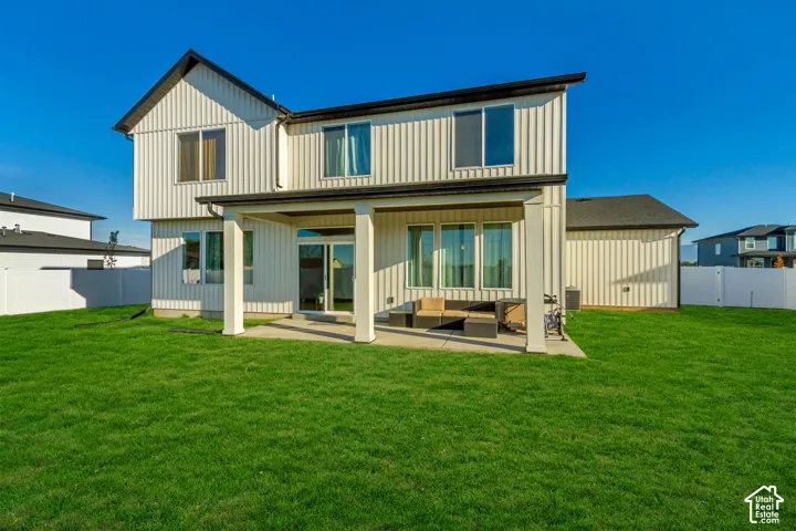 Expansive green lawn, covered patio, white vertical siding, dark roof, and multiple windows
