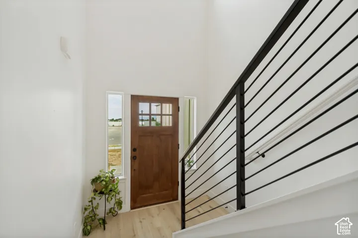 Vaulted entry, wood-finish flooring, wood entry door with glass panels, and modern horizontal bar railing