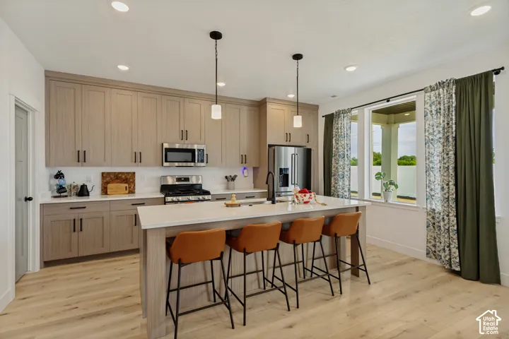 Recessed lighting, wood-finish flooring, light-toned cabinetry, stainless steel appliances, and a central island with countertop seating