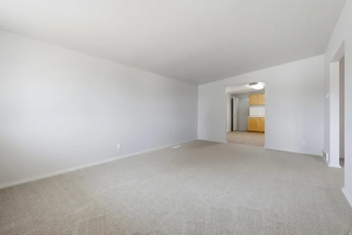 Spacious living area featuring light-colored carpeting and neutral wall tones