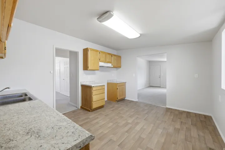 Kitchen featuring wood-finish flooring, light wood cabinetry, a double basin stainless steel sink, and light-toned countertops