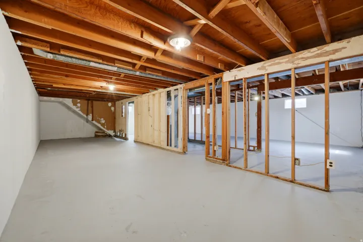 Unfinished basement featuring exposed wood ceiling joists, concrete flooring, and partial wall framing for customization