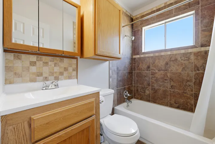 Bathroom featuring a white bathtub, ceramic tile shower surround, and a vanity with wood-finish cabinetry