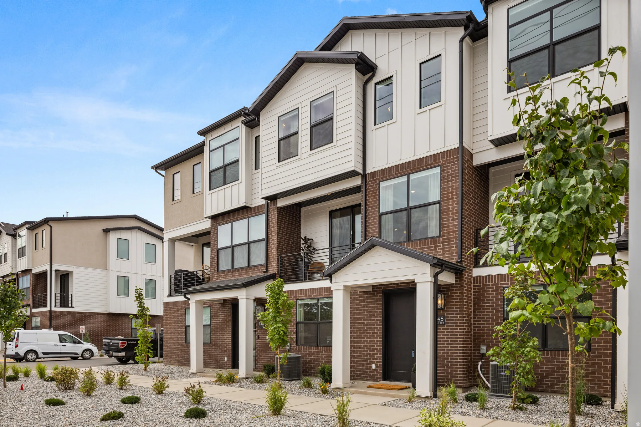 Contemporary exterior with brick and vertical white siding, large black-framed windows, prominent covered entry, and second-story balcony with metal railing