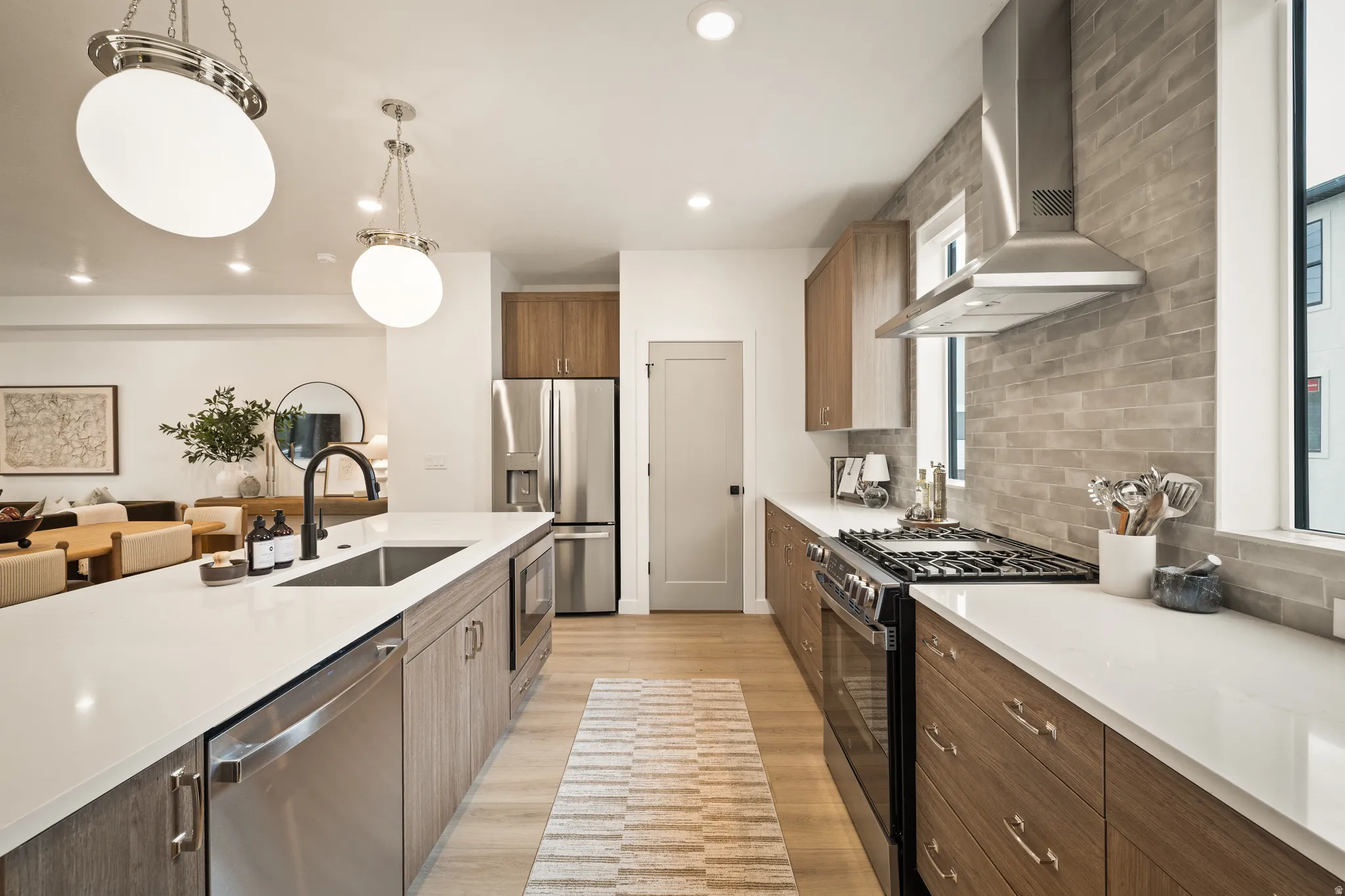Spacious kitchen featuring an elongated island with an undermount sink, stainless steel appliances, wood-finish cabinetry, and light-toned countertops