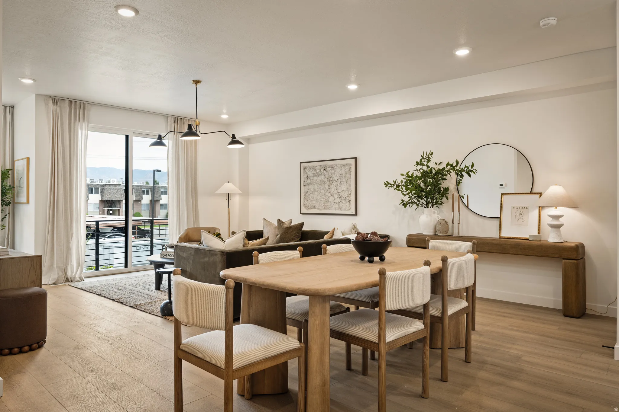 Recessed ceiling lighting, wood-finish flooring, full-height sliding glass doors, and a linear chandelier with three fixtures