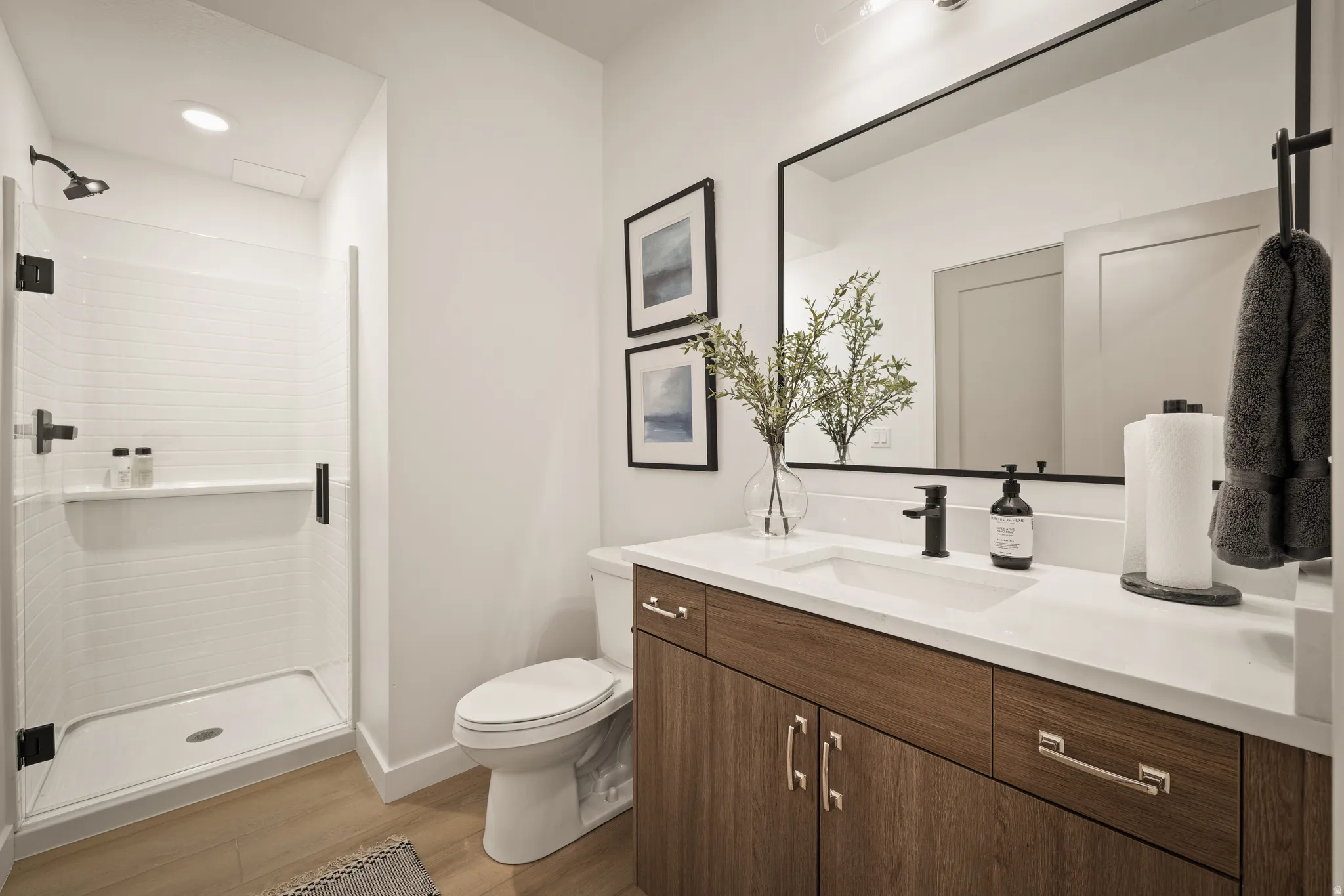 Walk-in shower with white subway tile, a single vanity with wood-finish cabinetry, a white countertop, and a large rectangular framed mirror