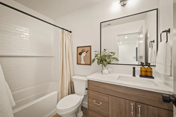 Tub/shower combination with subway tile surround, wood-finish vanity with an integrated sink, matte black hardware, and a large framed mirror