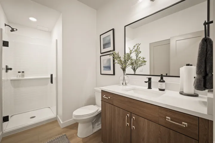 Walk-in shower with white subway tile, a single vanity with wood-finish cabinetry, a white countertop, and a large rectangular framed mirror