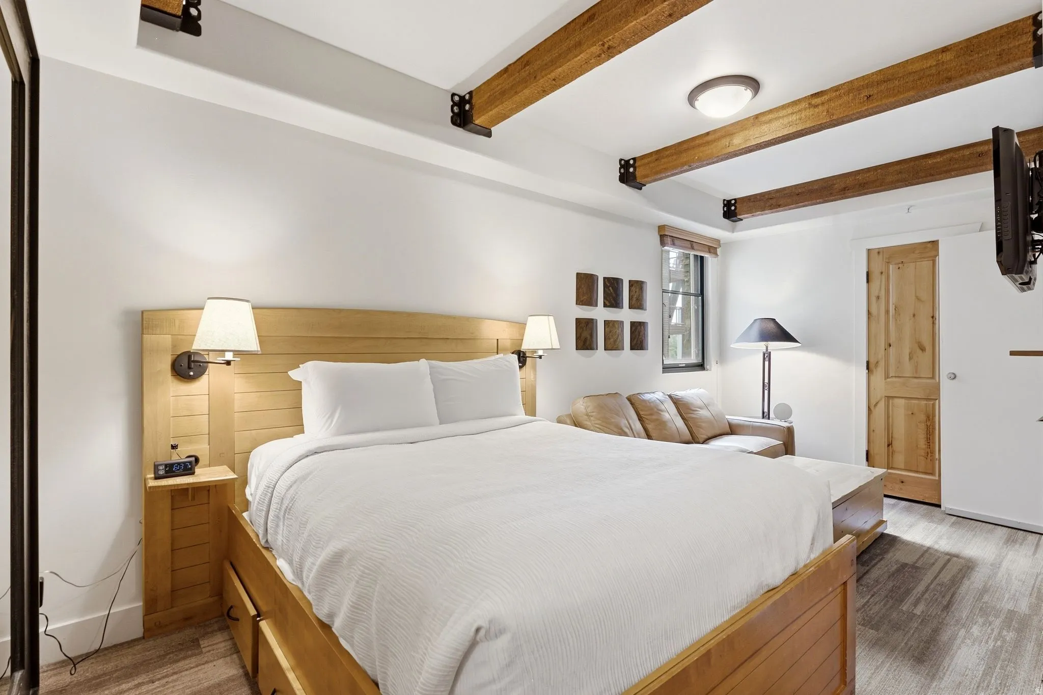 Exposed wood beams, wood-finish flooring, built-in bedside lighting, and a wood-paneled door