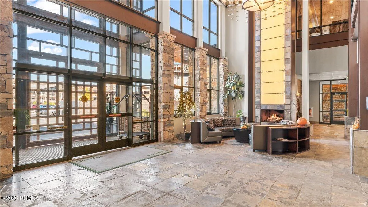 Grand entrance with expansive window walls, stone-clad columns, a floor-to-ceiling fireplace, and large format stone flooring