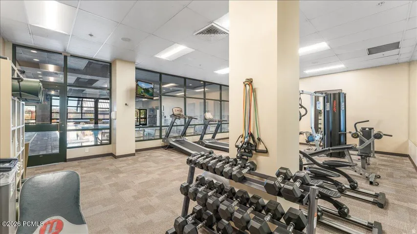 Dedicated fitness area featuring patterned carpet flooring, extensive glass paneling, a full-height column, and recessed lighting