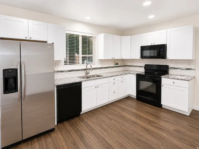 Kitchen with wood-finish flooring, white cabinetry, integrated stainless steel refrigerator, black appliances, and granite countertops