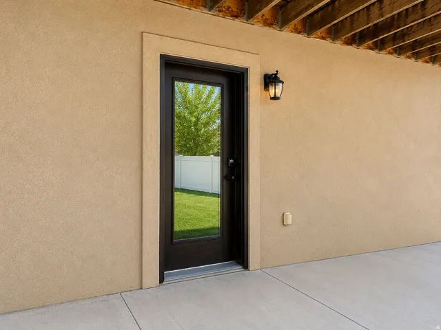 Stucco exterior with a full-light panel door, exterior wall lantern, and concrete patio