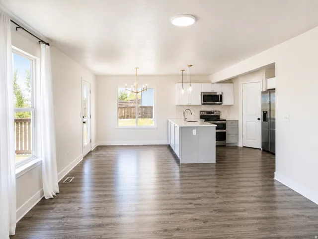 Open-concept living space with wood-finish flooring, white cabinetry, stainless steel appliances, and a central island with a sink