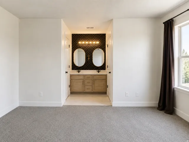 Dual vanity with wood-finish cabinetry, black tile backsplash, and two framed oval mirrors