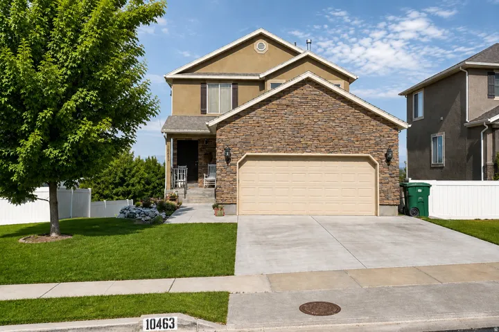 Stucco and stone exterior, two-car garage, mature landscaping, concrete driveway, and front entryway