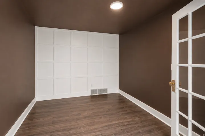 Wood-finish flooring, accent wall with decorative paneling, recessed ceiling light, and glass-paneled door
