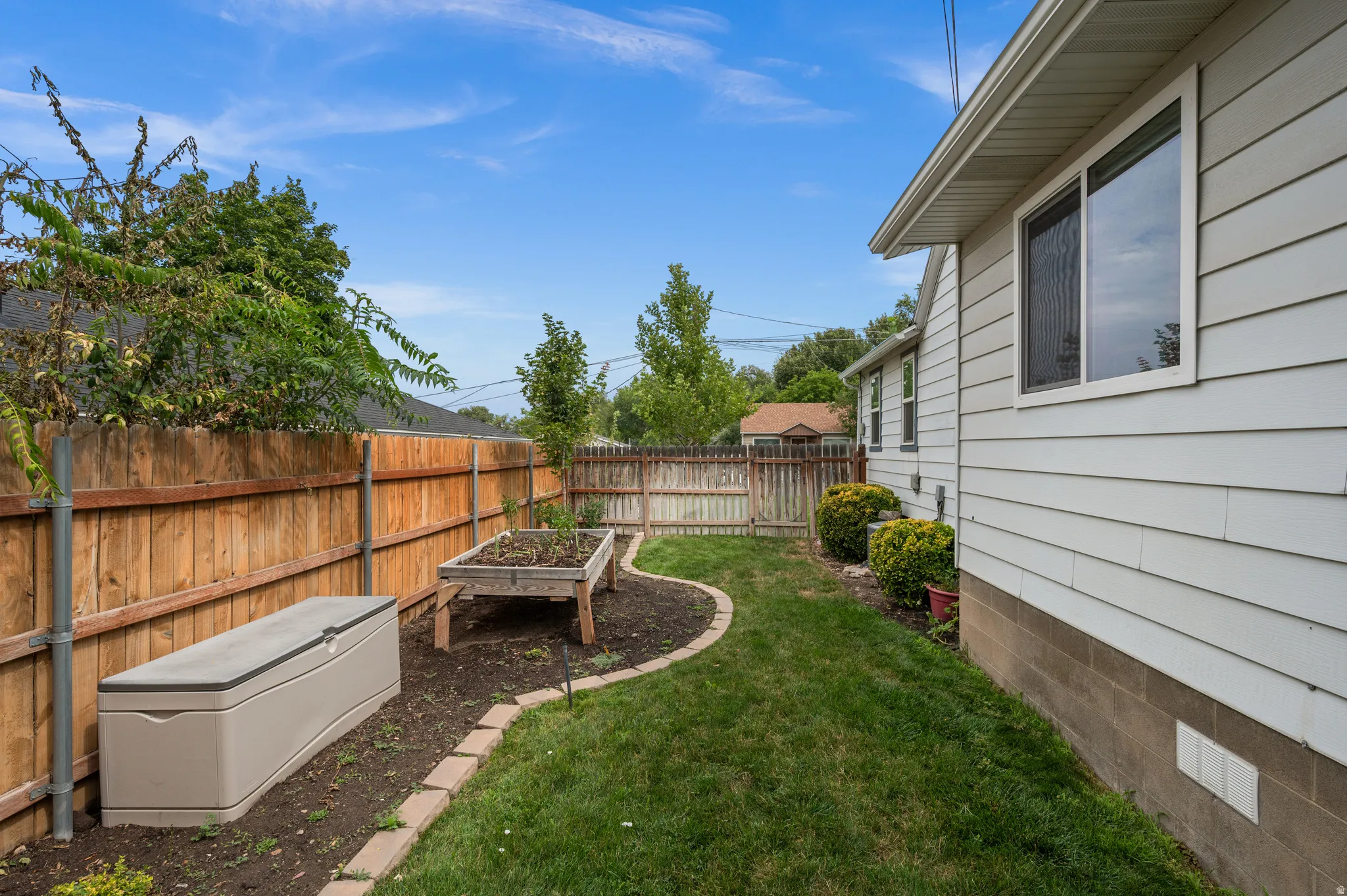 Side yard featuring a wood privacy fence, raised garden bed, and manicured lawn