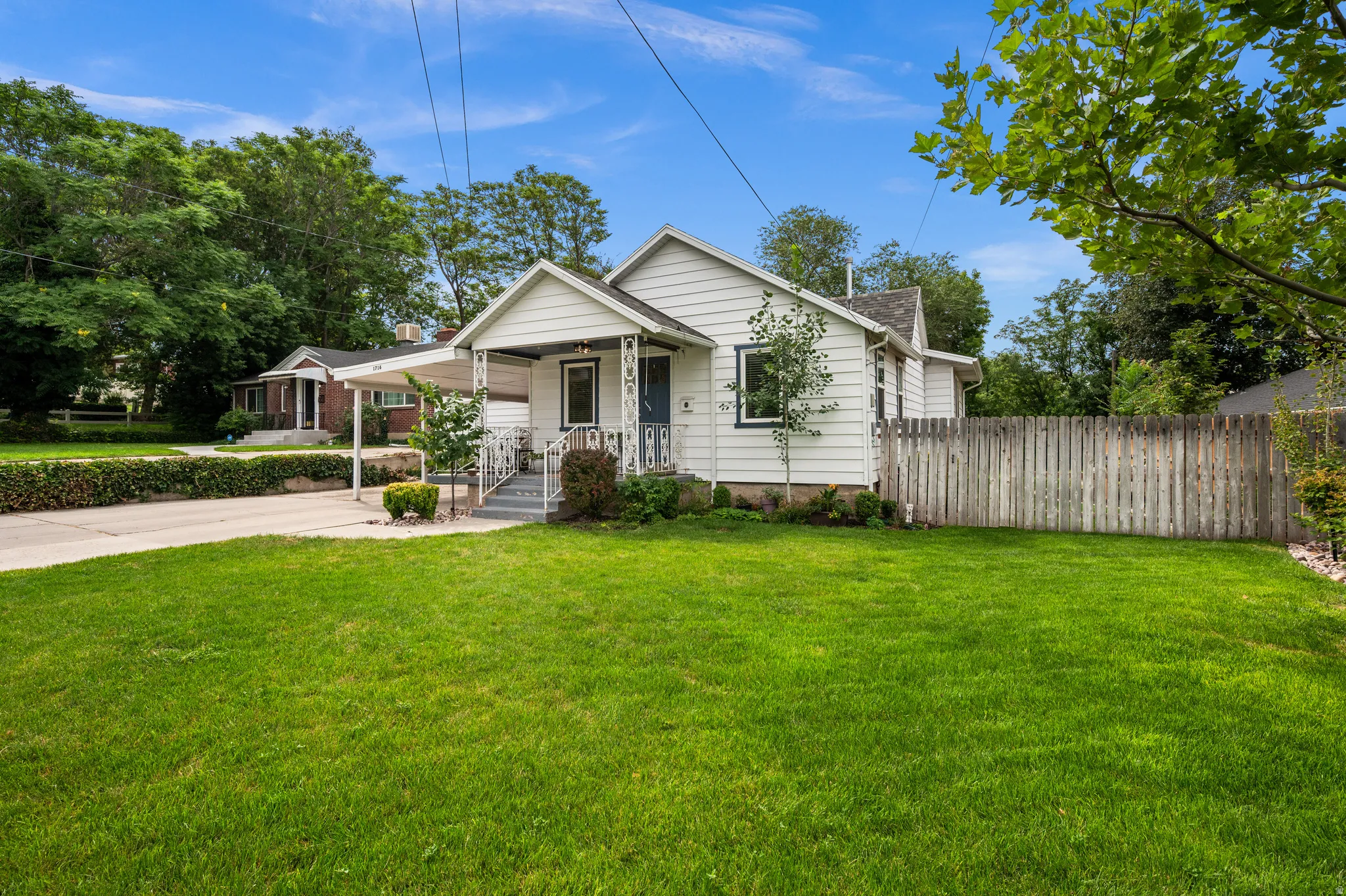White siding exterior, covered front porch, carport, mature landscaping, and a fenced side yard