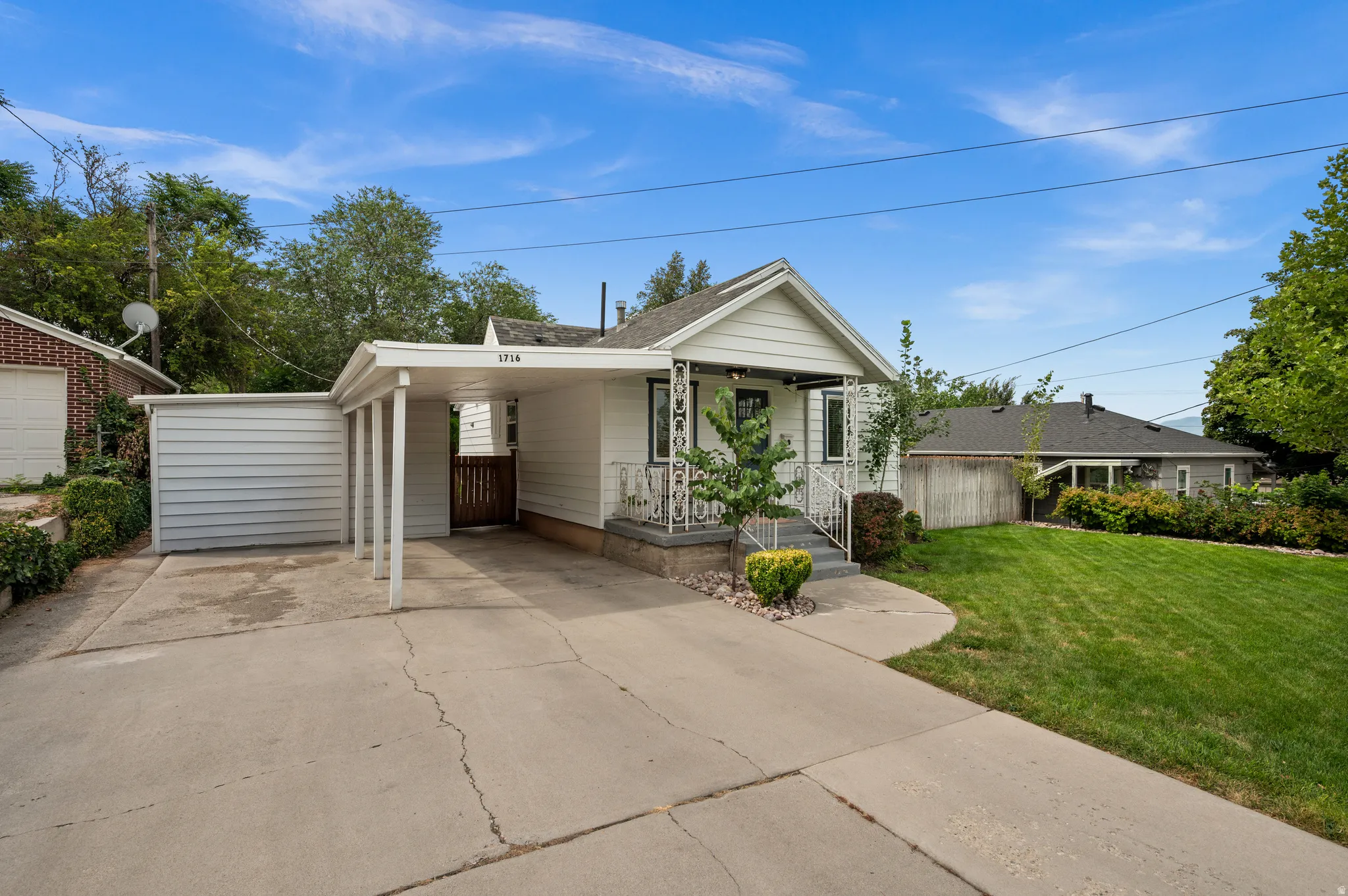 White siding exterior with a covered carport, concrete driveway, and front lawn