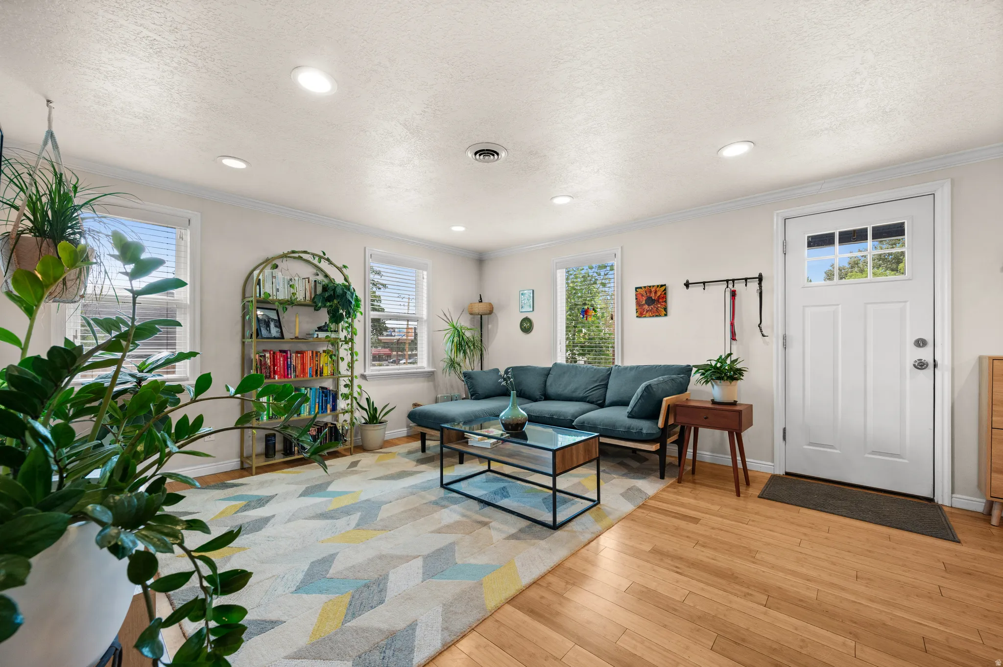 Wood-finish flooring throughout, recessed lighting, crown molding, multiple windows with blinds, and a white entry door with frosted glass panes