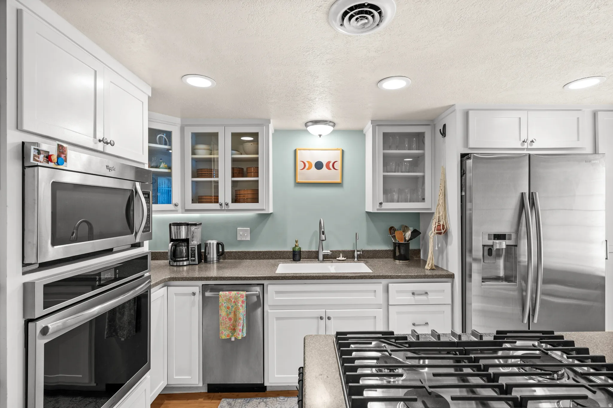 White cabinetry, stainless steel appliances, recessed ceiling lighting, undermount sink, and solid surface countertops