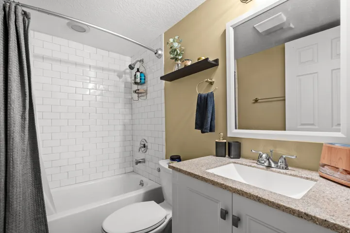 Bathroom featuring a white subway tile tub surround, built-in bathtub, white vanity with a light-toned countertop, under-mount sink, and framed mirror