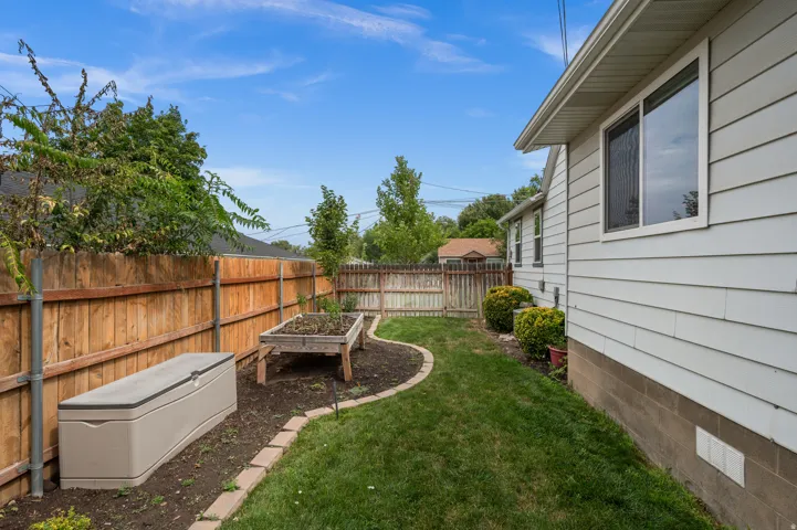 Side yard featuring a wood privacy fence, raised garden bed, and manicured lawn