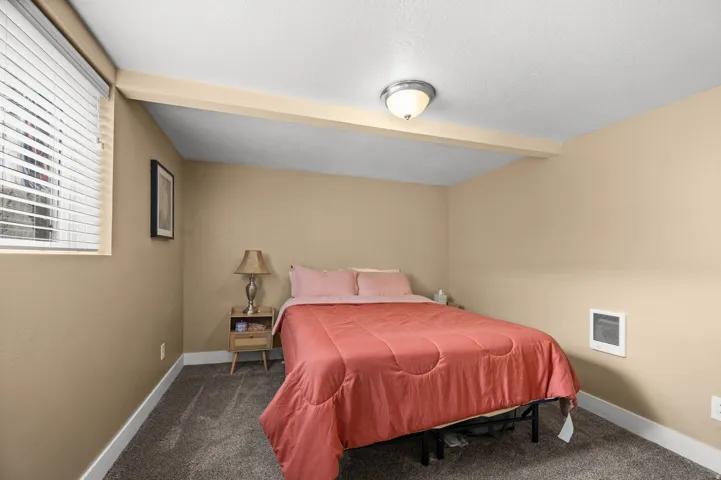 Carpeted flooring, neutral wall color, window with blinds, ceiling-mounted light fixture, and wall-mounted heating unit