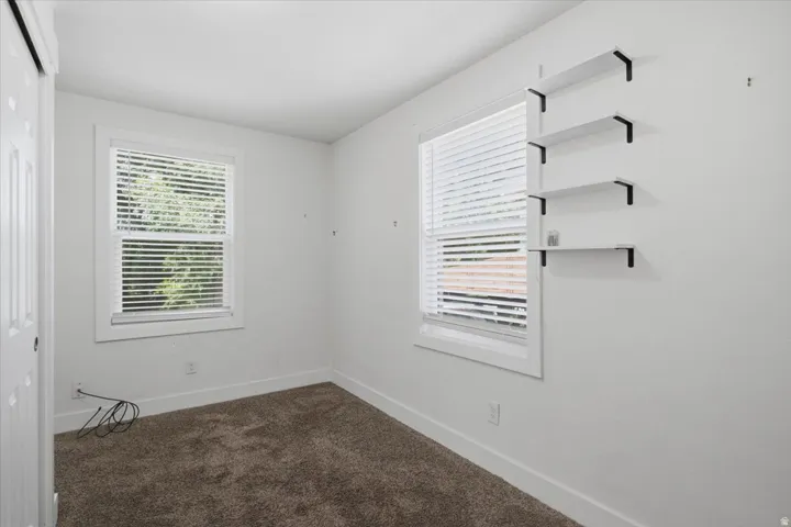 Neutral wall color, two windows with blinds, built-in shelving, white trim, and carpeting