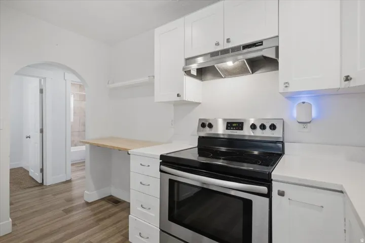 White cabinetry, light countertops, wood-finish flooring, stainless steel range, and stainless steel range hood