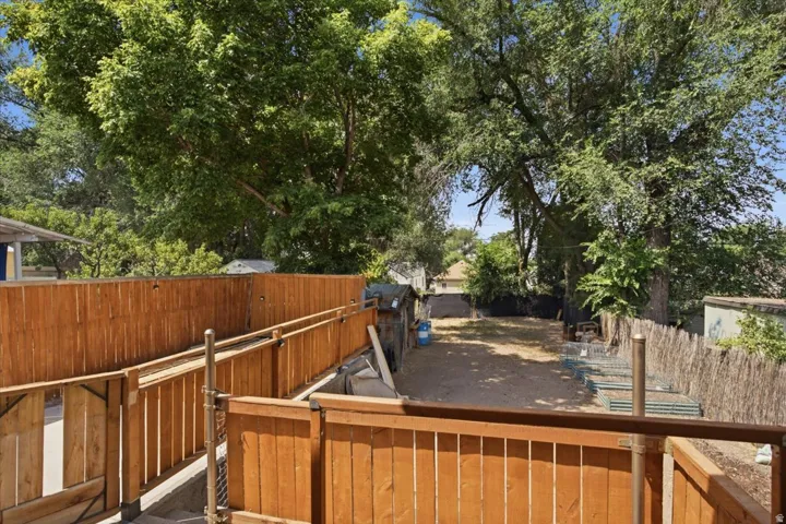 Spacious outdoor area featuring a wooden privacy fence, mature trees, and a wooden ramp with railings