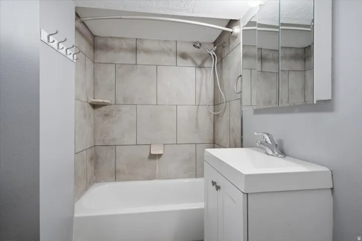 Bathtub with tile surround, showerhead, wall-mounted storage, and vanity with integrated sink