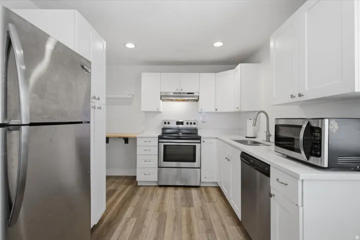 Kitchen featuring white cabinetry, light countertops, wood-finish flooring, and stainless steel appliances