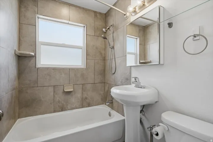 White pedestal sink, modern chrome faucet, and tiled shower surround with an integrated soap dish