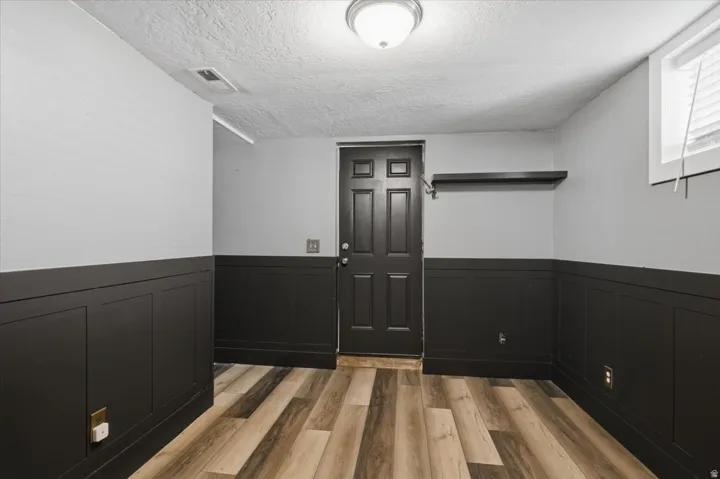 Wood-finish flooring, half-wall wainscoting, solid paneled door, and a built-in wall shelf