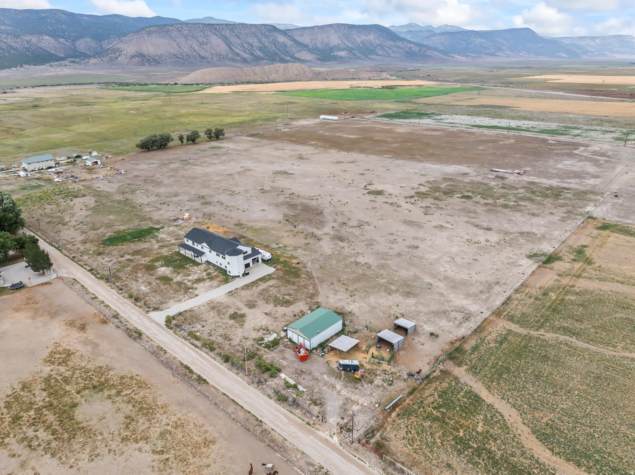 Expansive rural property featuring a white multi-story residence, a green outbuilding, multiple agricultural structures, and a gravel drive