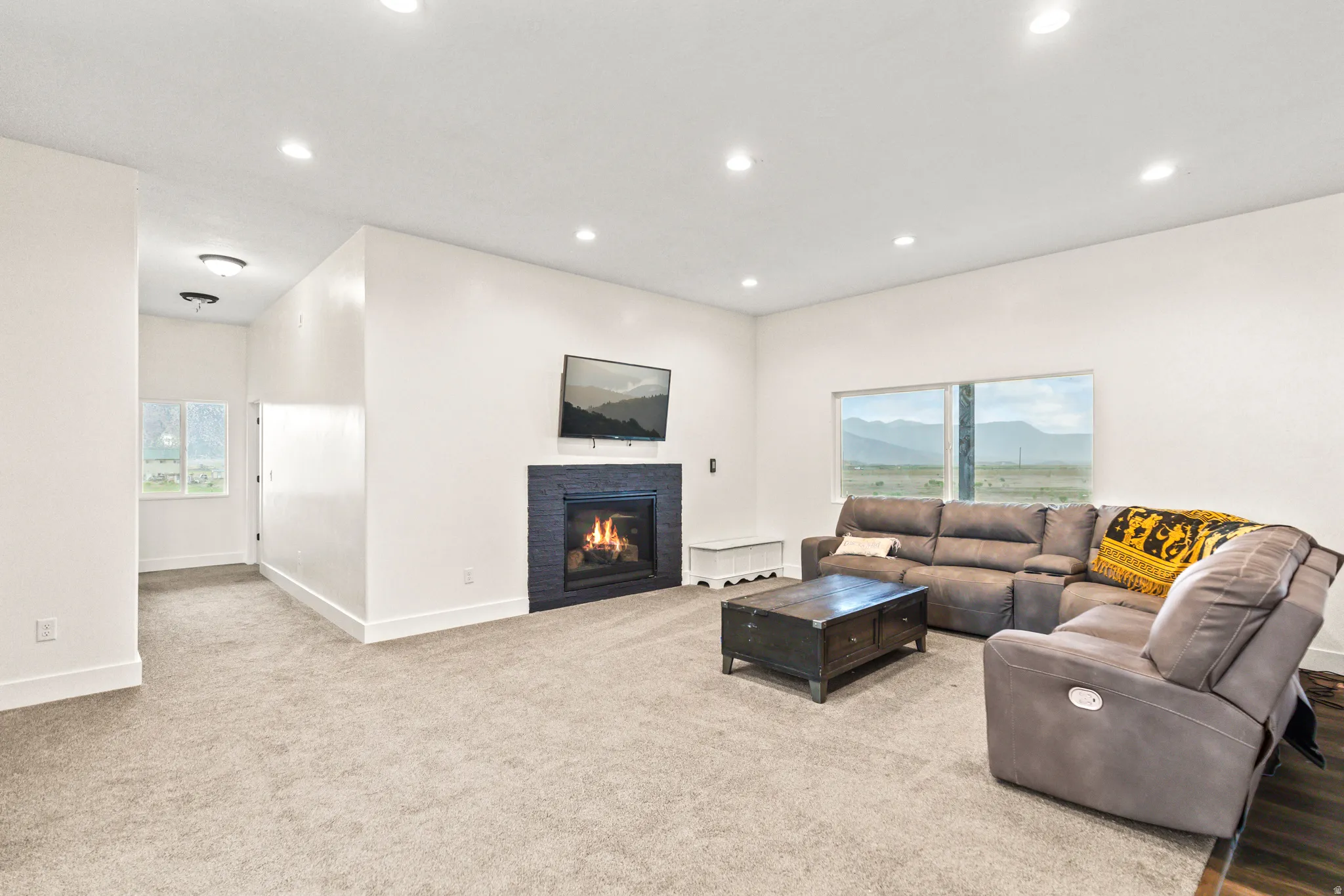 Recessed ceiling lighting, tiled fireplace surround, integrated wall-mounted television, large windows, and neutral carpet