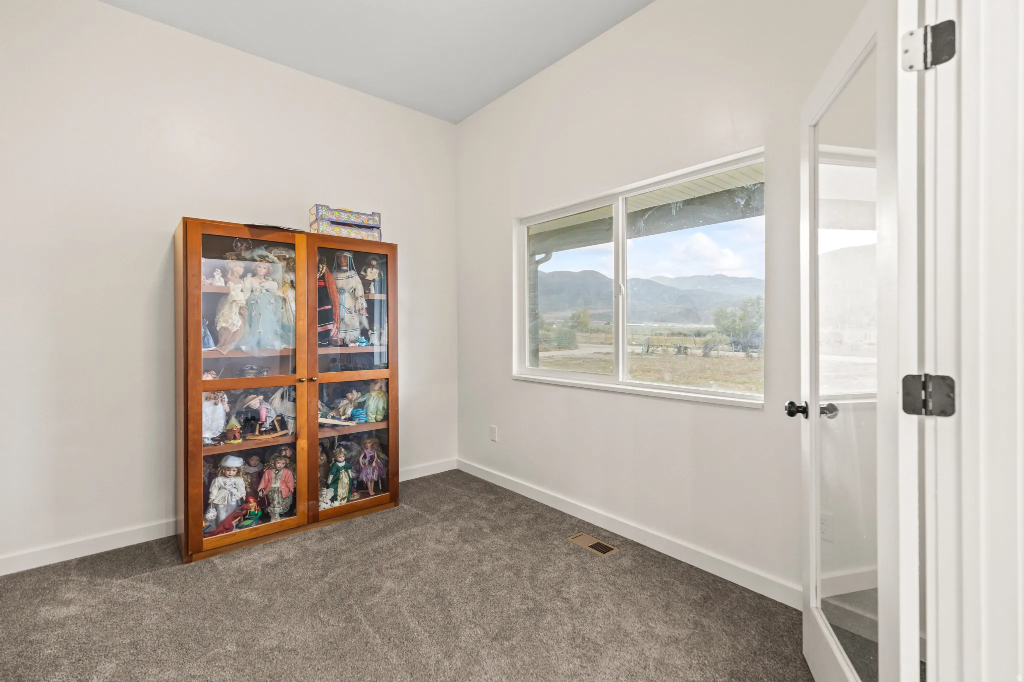 Vaulted ceiling, white walls, gray carpet flooring, white-framed window, glass-paneled door